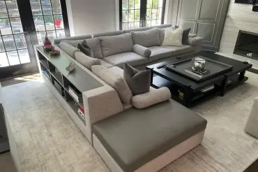 Elegant grey custom upholstered L shaped sectional with bolster pillows and a built in custom bookcase attached to the back of the sectional.