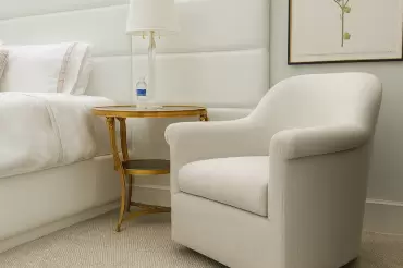 A wall-mounted white leather bed and extended headboard complete the epansive look of this glamorous Florida primary bedroom. Our bespoke club chair is the cherry on top!